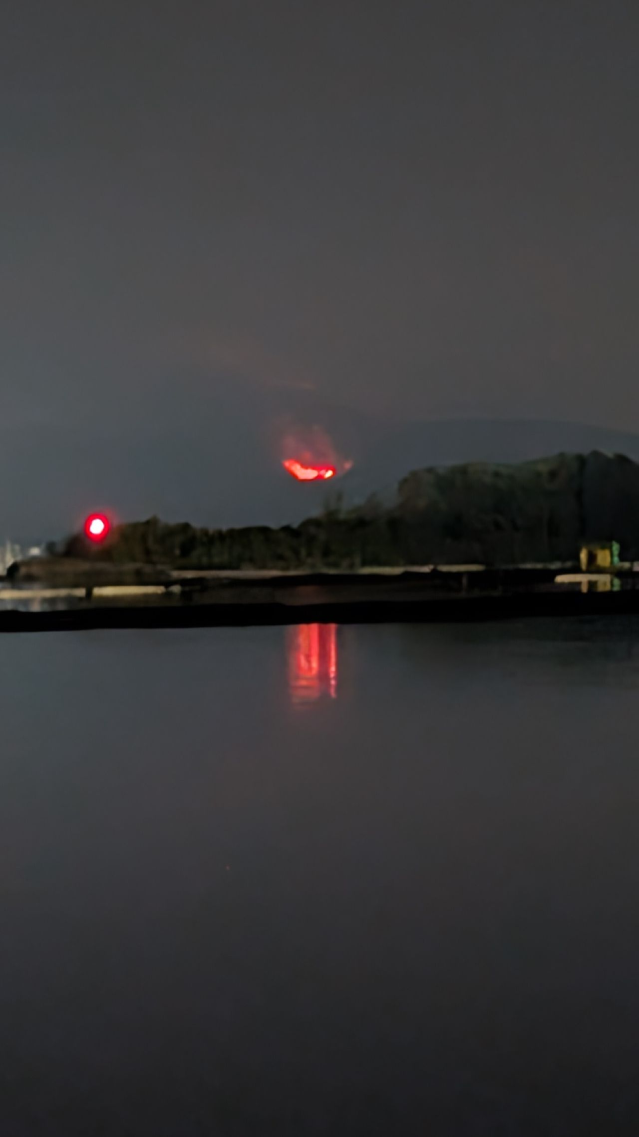 Wildfire burning on a hillside at night with flames reflected in the still water of Ladysmith Harbour