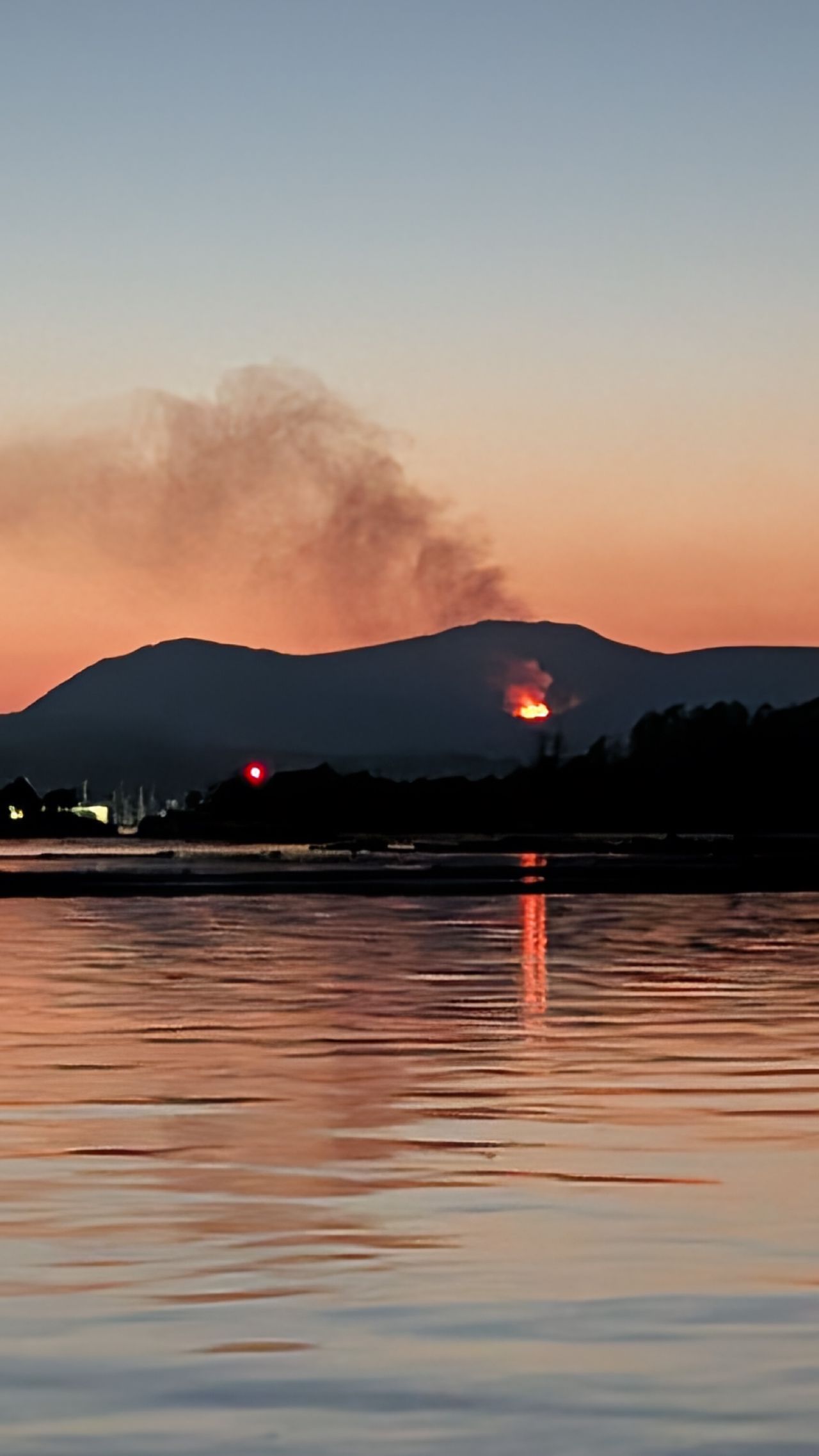 Wildfire glowing orange on a distant mountain with smoke rising into the sunset sky over Ladysmith Harbour