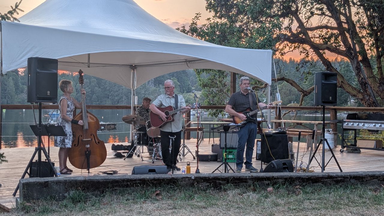 Four-piece band performing on an outdoor stage at sunset during the Telegraph Harbour rendezvous