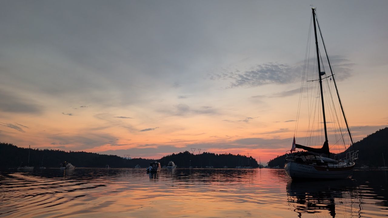 Sailboats silhouetted against a glowing sunset sky reflected in the calm waters of Montague Harbour