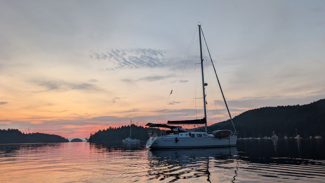 SV Yahara at anchor in Montague Harbour with a colorful pink and orange sunset and scattered clouds