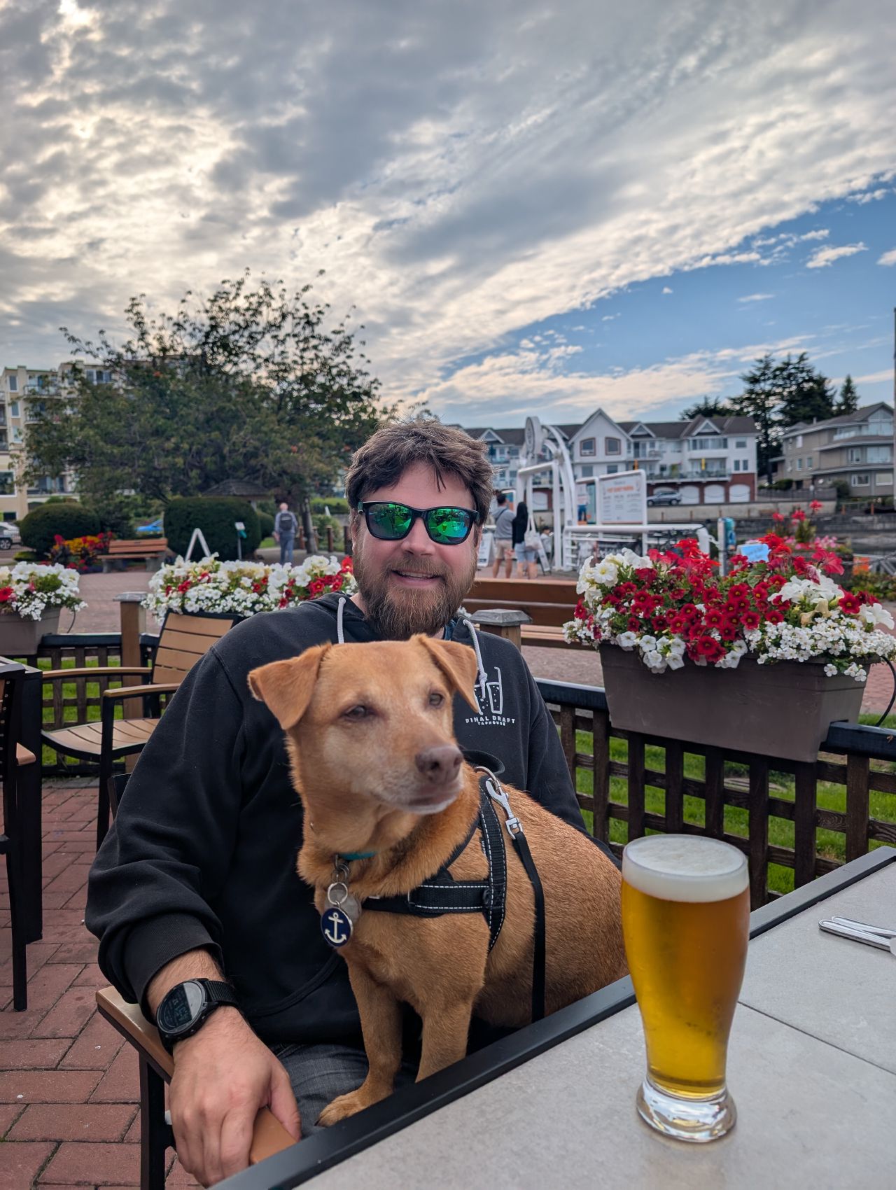 Brian and Maui sitting at a waterfront patio with a pint of beer and flowers in Sidney