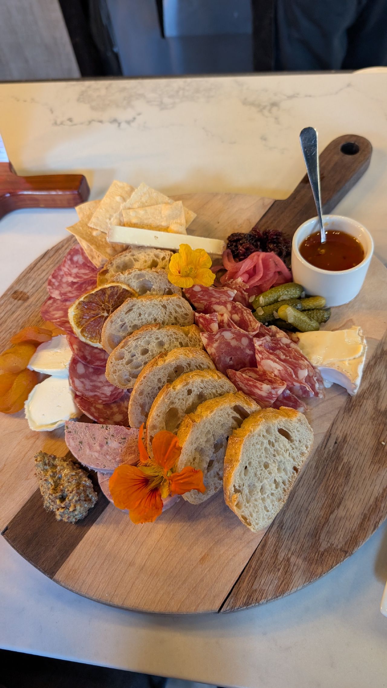 Beautiful charcuterie board with sliced bread, cured meats, cheese, cornichons, and edible flowers