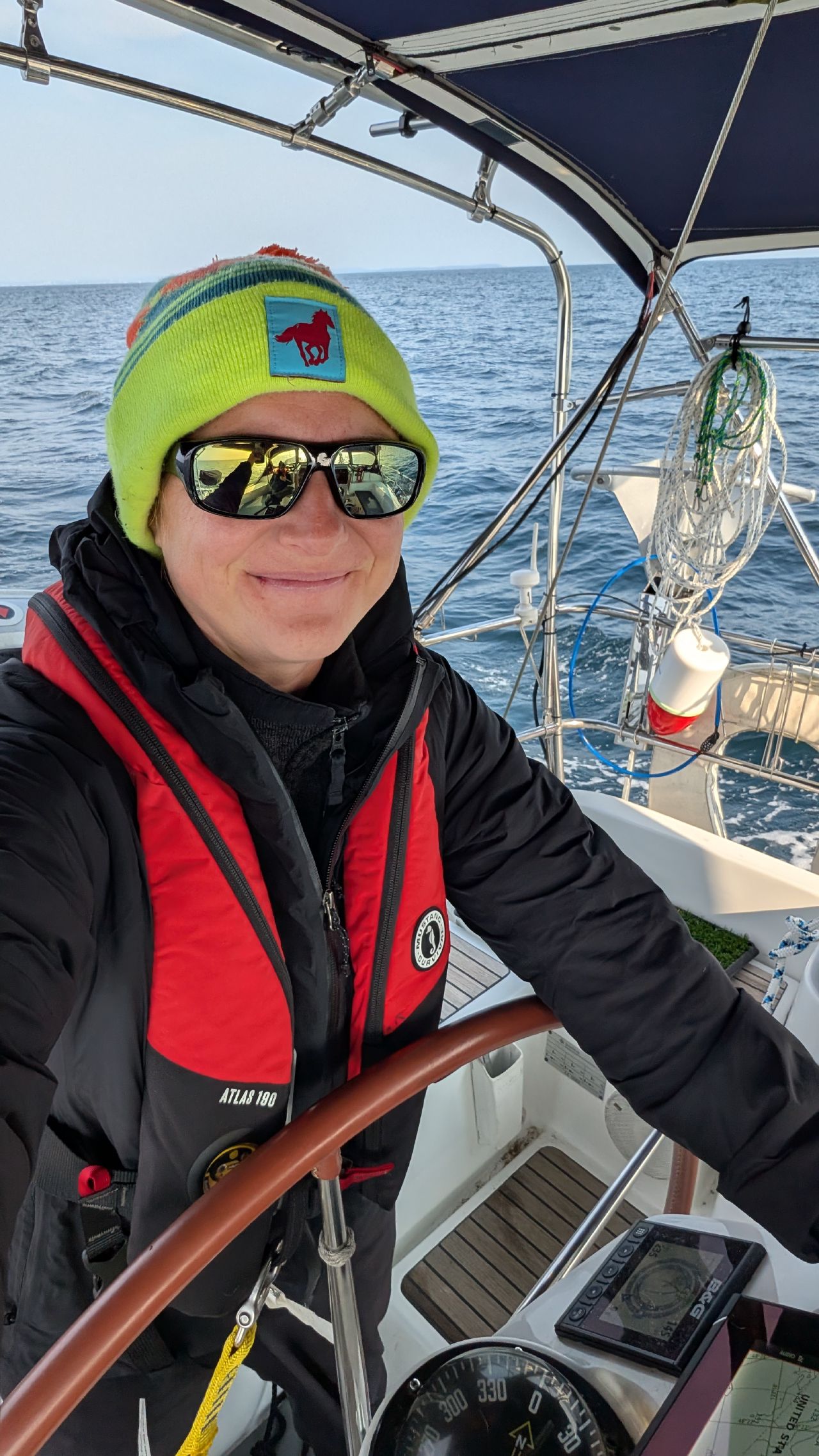 Rachel at the helm in a colorful beanie and life jacket crossing the Strait of Juan de Fuca