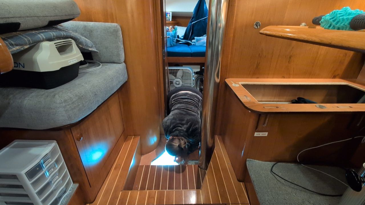 Rachel crawling through the cabin with a flashlight to trace the source of a water leak