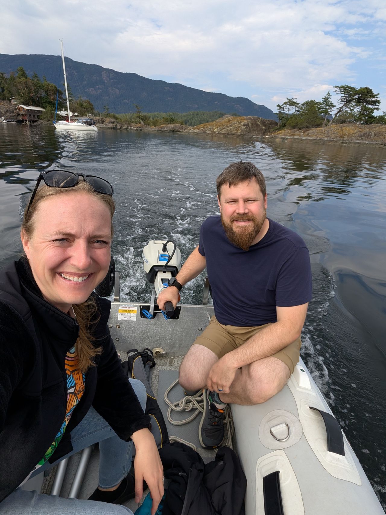 37% 51% Rachel and Brian riding the dinghy near the anchorage, sailboat behind