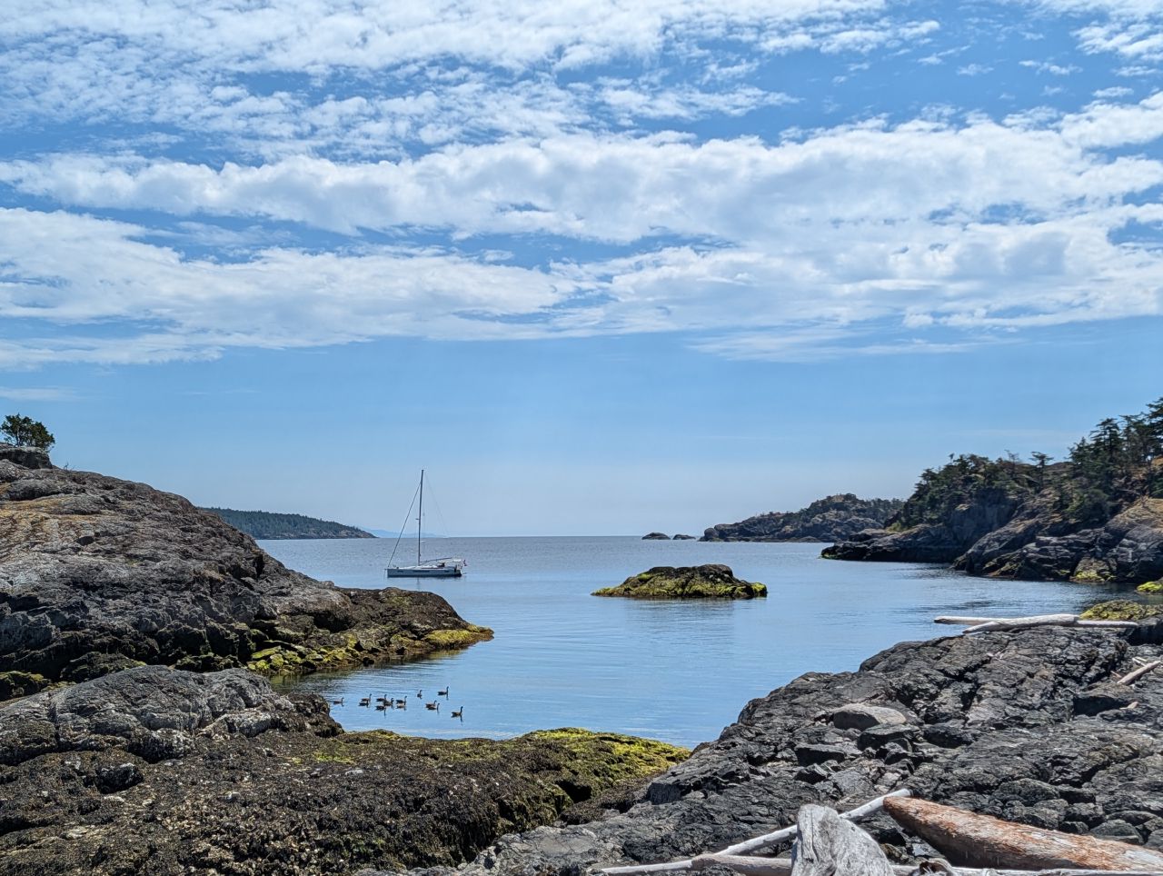 The sailboat anchored in a calm cove, seen from the rocky shore