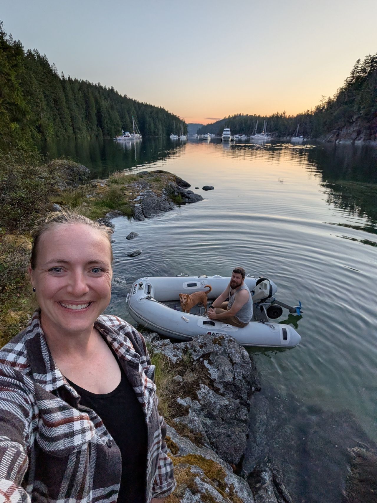 Rachel on the rocky shore at sunset with Brian in the dinghy
